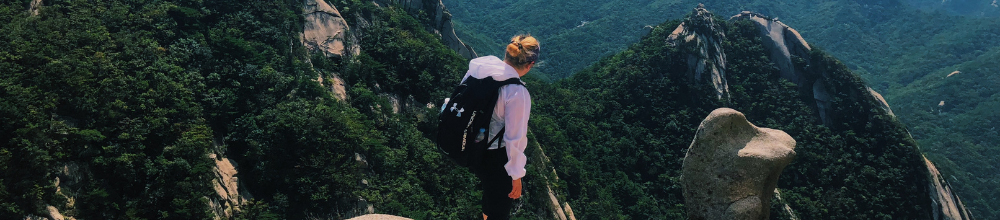 Girl stands on green mountain with her back to the camera